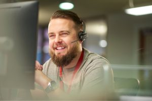 A male who is smiling looking at his computer screen with a headset on