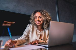 A woman sitting at a desk with her laptop in front of her and a pen in her hand.