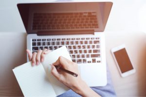 This is an image of a birds eye view of a laptop and notebook along with a pen