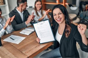 Colleagues seated around a desk with a contract displayed and one person smiling at camera