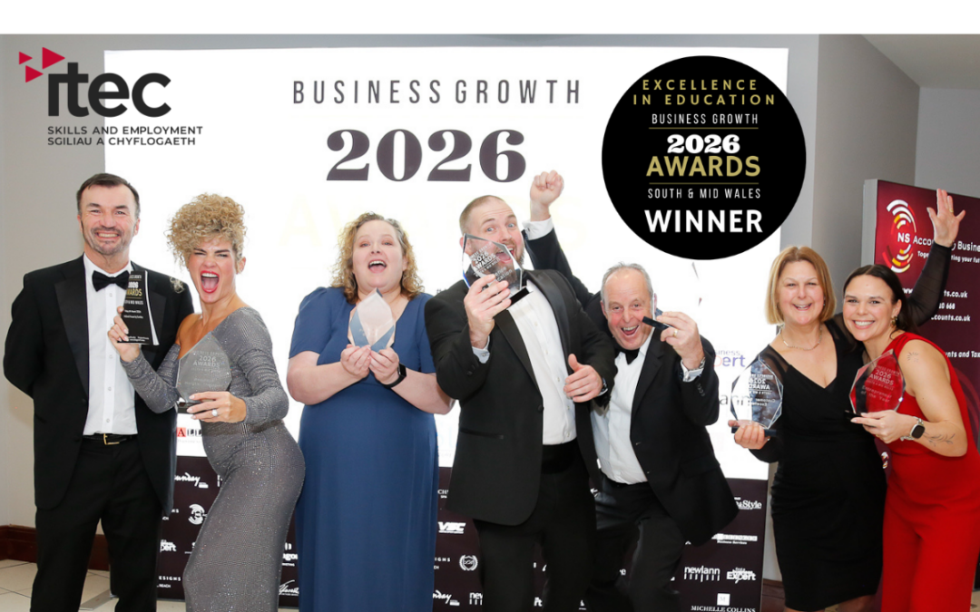 A group of six people dressed in formal evening wear stand together, smiling and holding glass awards. They pose enthusiastically in front of a backdrop displaying the ITEC logo and text reading “Business Growth 2026” and “Excellence in Education Business Growth 2026 Awards South & Mid Wales Winner.”